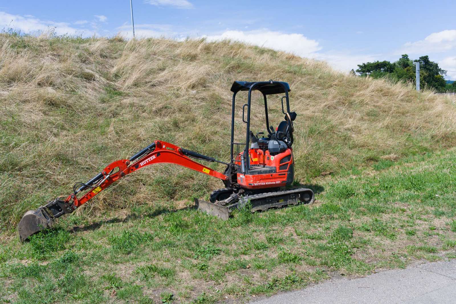Compact excavator parked on a grassy bank at a residential job site